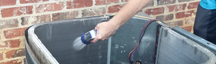 HVAC technician cleaning condenser coils during a maintenance visit