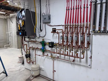 Wall-mounted boiler feeding a copper and red PEX radiant heating manifold