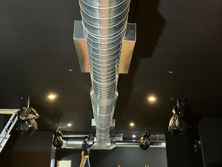 Polished spiral duct dropping through the ceiling of a dark modern interior
