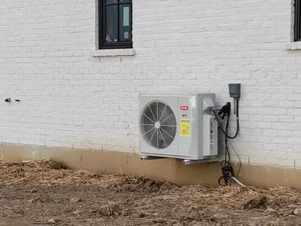 Outdoor heat pump unit mounted against the white brick exterior of a home