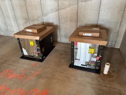 Two new heating units set on pads in a poured-concrete mechanical room, ready for connection