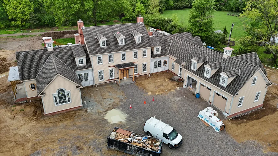 Aerial view of a newly built custom home during final construction, with a work van and materials on site