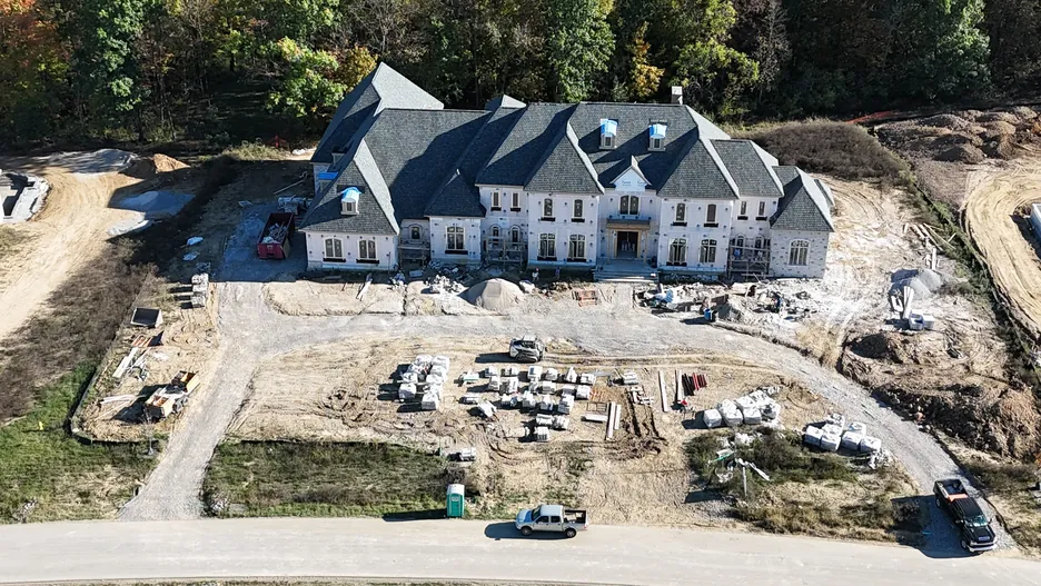 Aerial view of a new custom home nearing exterior completion, with graded site work and staged materials