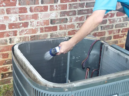 Technician cleaning the coil fins of an outdoor air conditioning condenser during a maintenance visit