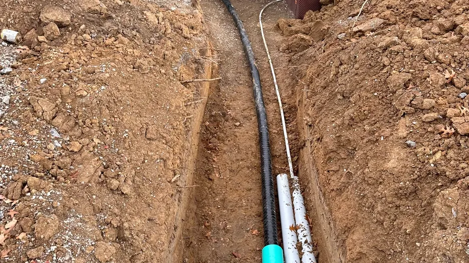 Insulated radiant heating supply lines being installed in a trench before backfill